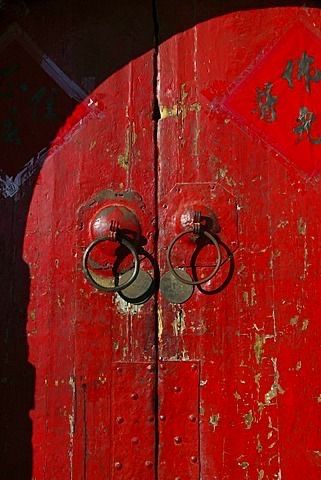 Une porte rouge patinée avec deux heurtoirs circulaires.