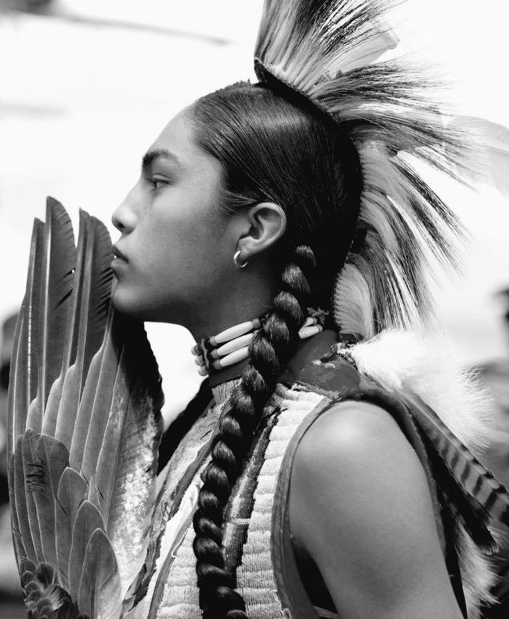 Portrait de profil en noir et blanc, cheveux tressés et parure de plumes.
