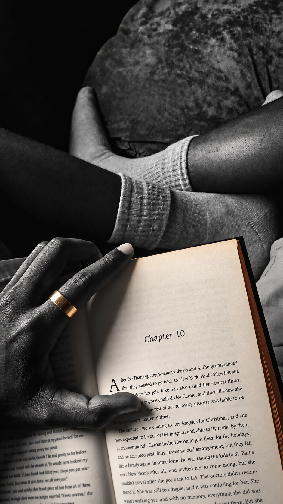 Main sur un livre ouvert, photo en noir et blanc avec pages ivoire et bague dorée.